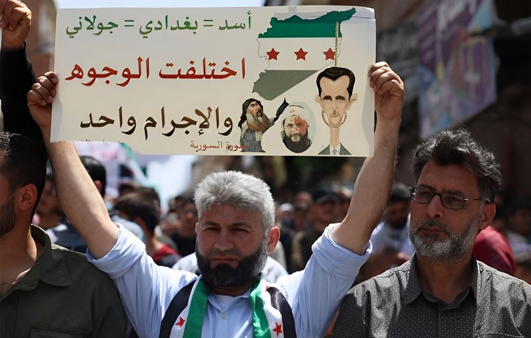 A protester at an anti-Hayat Tahrir al-Sham rally in Binnish, Idlib province, May 17, 2024. The sign reads: “Assad = Baghdadi = al-Jolani. Different faces, same crime.”